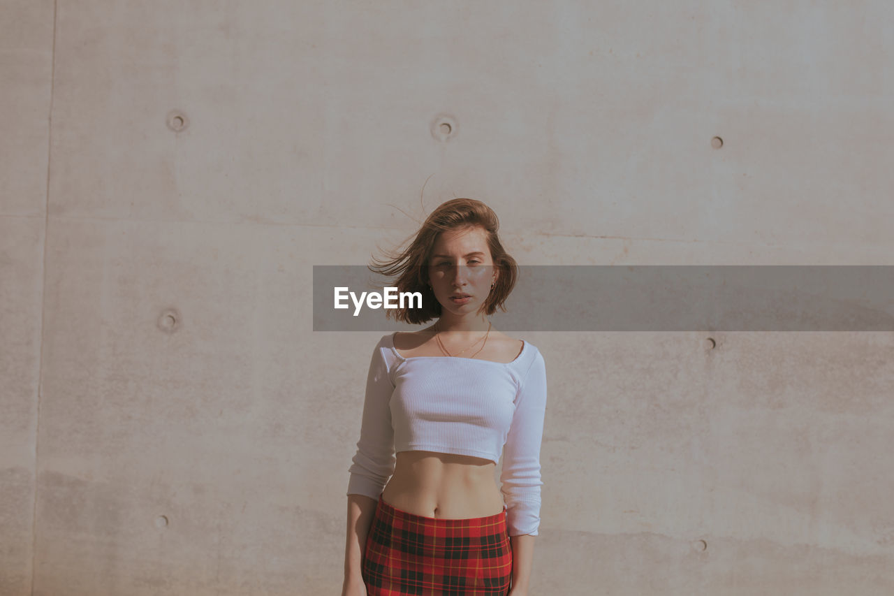 Portrait of young woman standing against wall