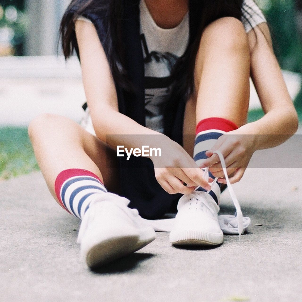 Low section of young woman tying shoelace while sitting on footpath