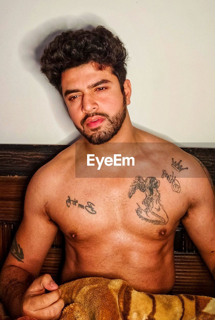 PORTRAIT OF SHIRTLESS YOUNG MAN STANDING AT HOME