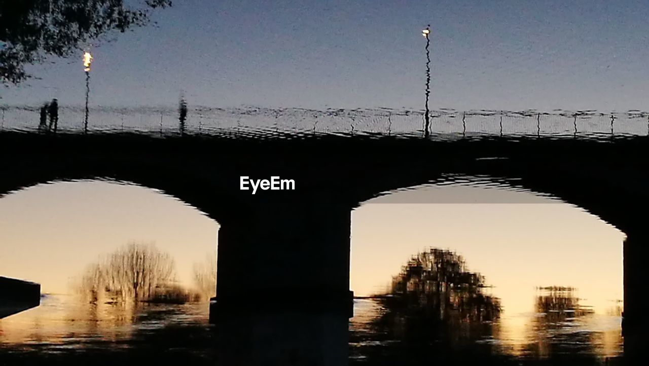 Silhouette bridge over river against sky at sunset