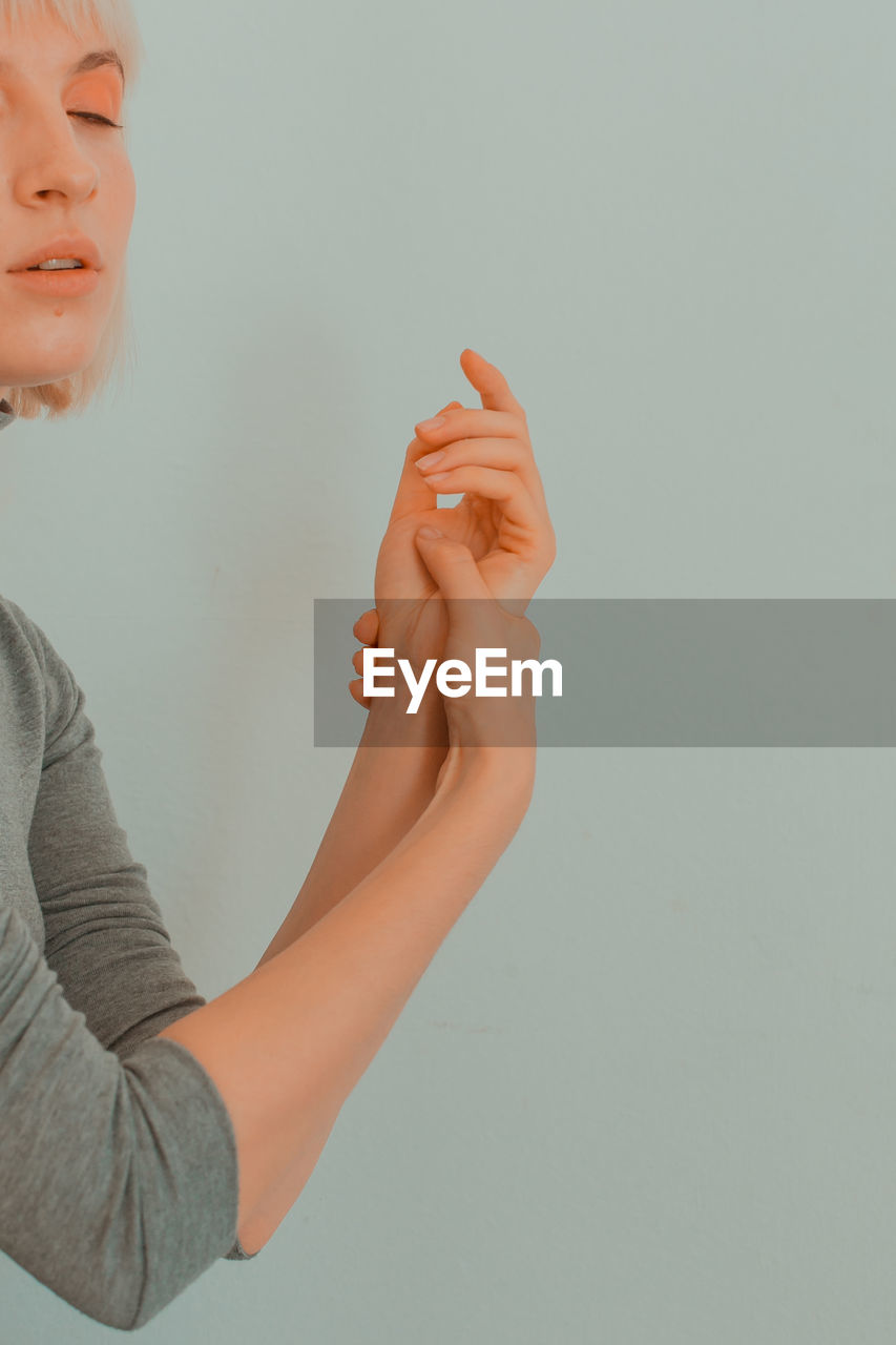 Young woman with eyes closed massaging her hand against white background