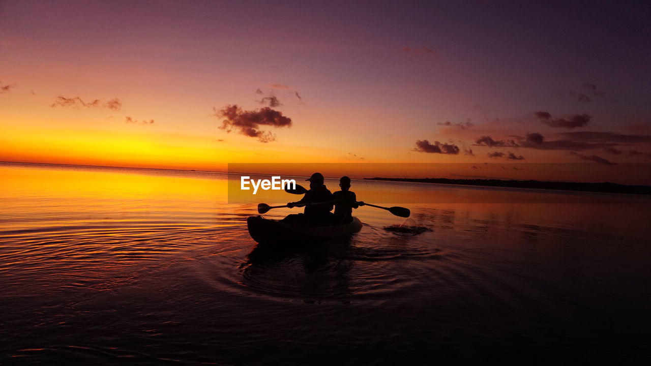 Silhouette people rowing boat in sea against sky during sunset