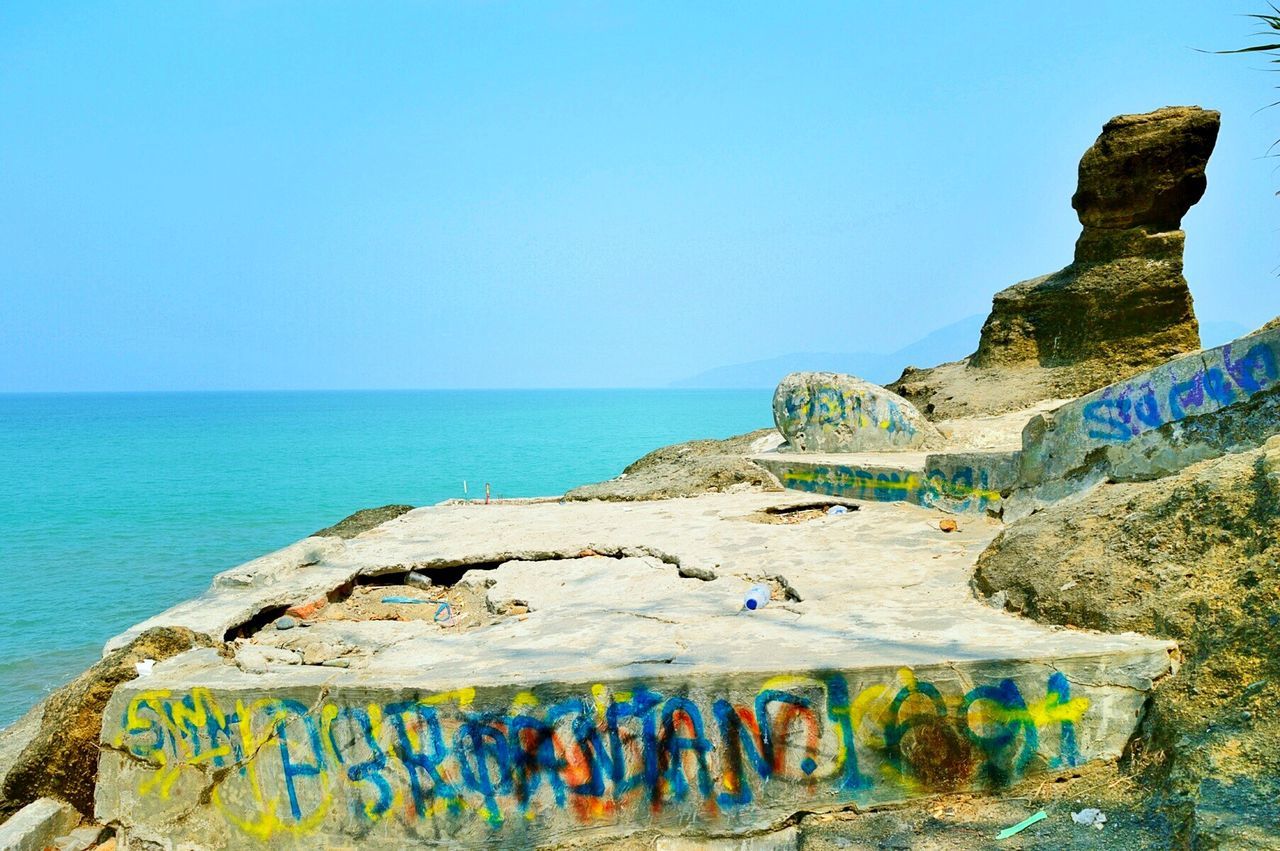 Graffiti on rock formation by sea against clear sky