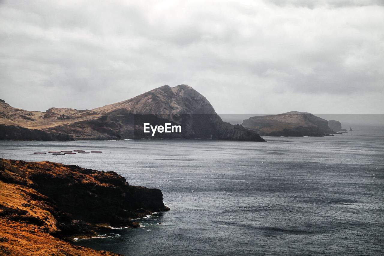 Rock formations on sea against cloudy sky