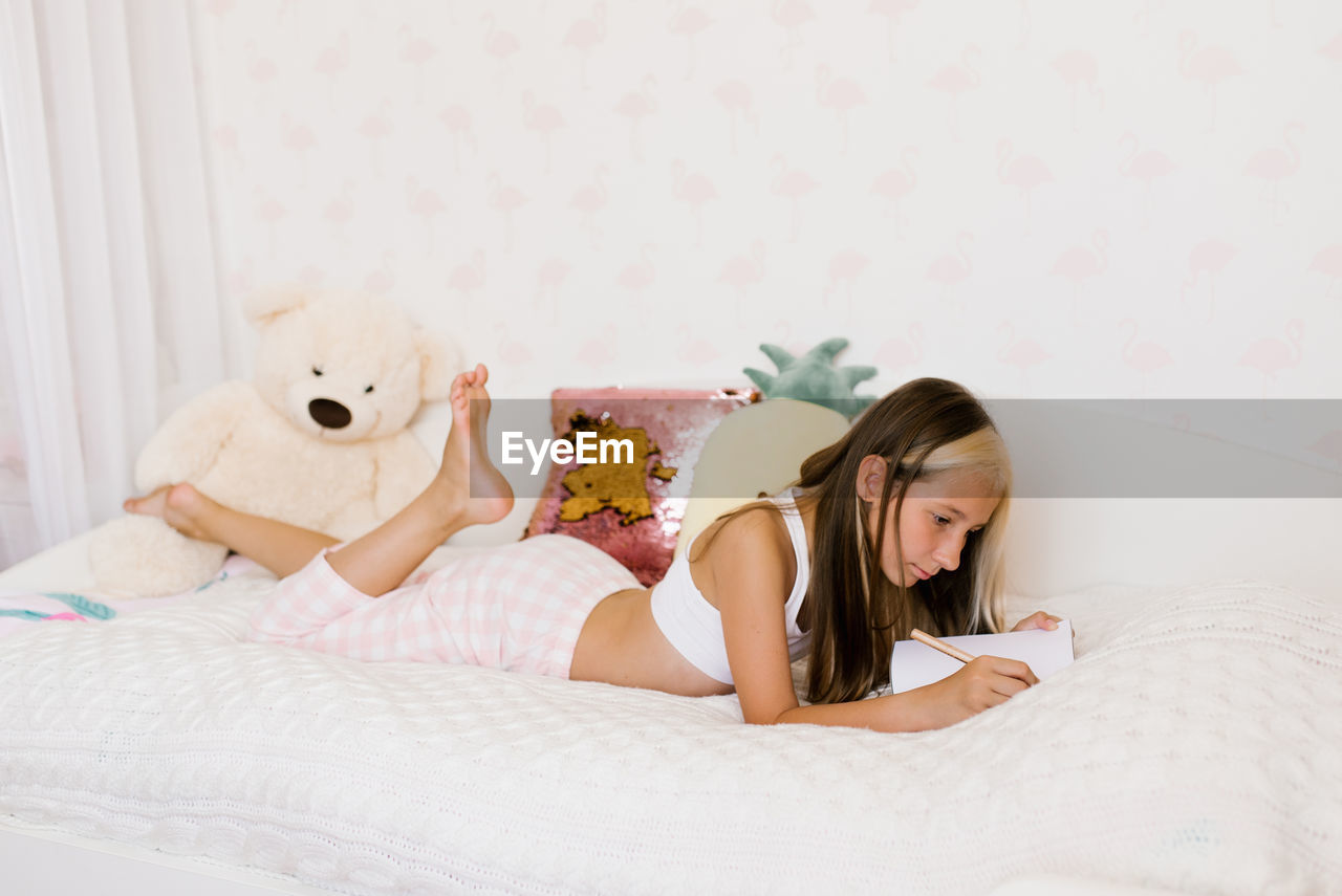 portrait of young woman using mobile phone while lying on bed at home