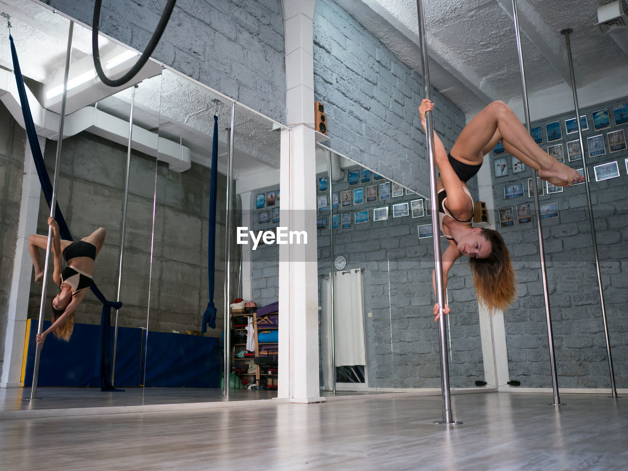 Sensuous woman practicing pole dance reflecting on mirror in studio