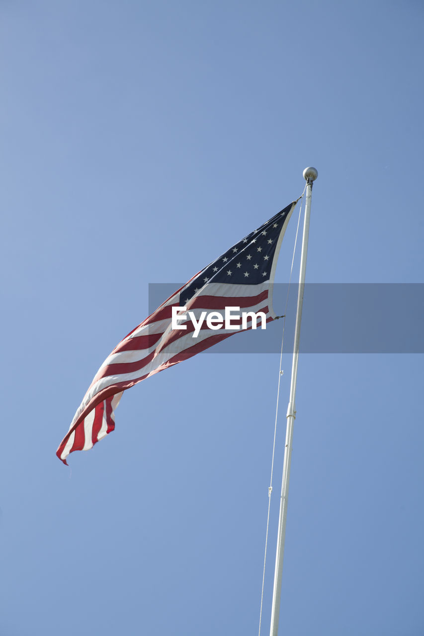 Low angle view of flags against clear blue sky