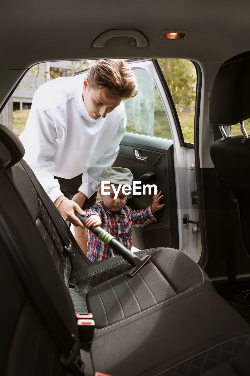 Man with toddler son vacuum cleaning car