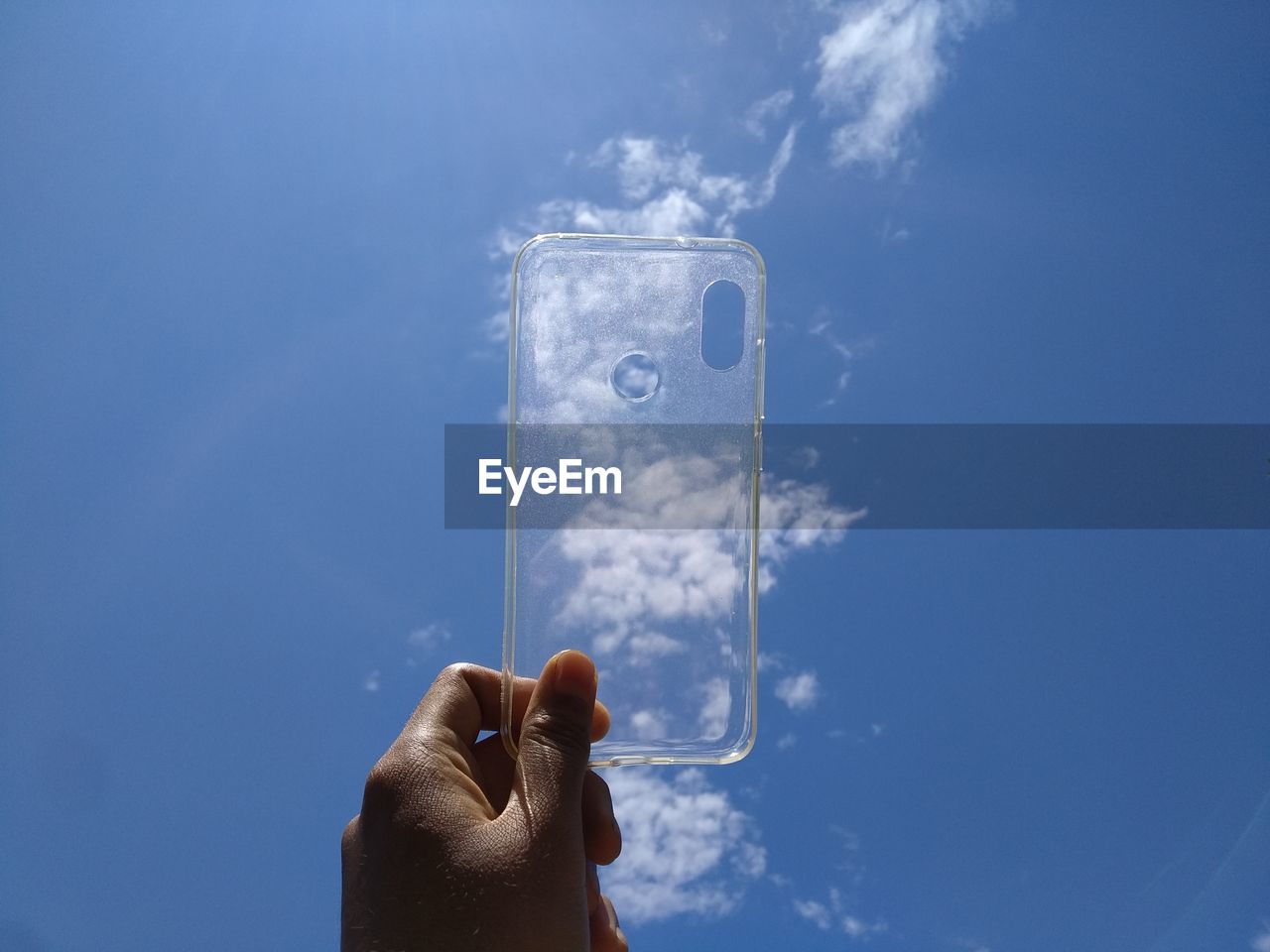 Person holding phone case against blue sky