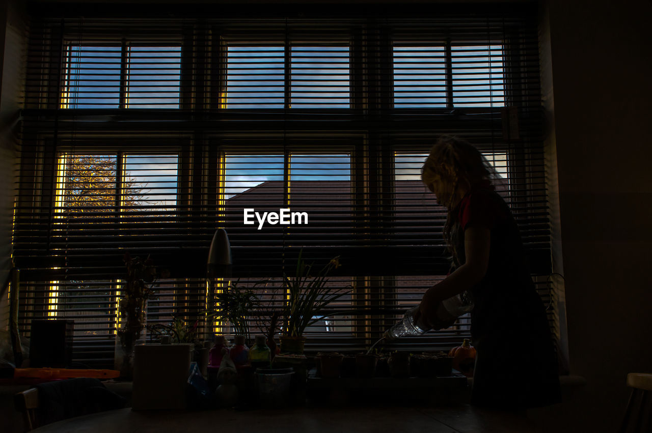 Woman pouring drinking water at dining table by window