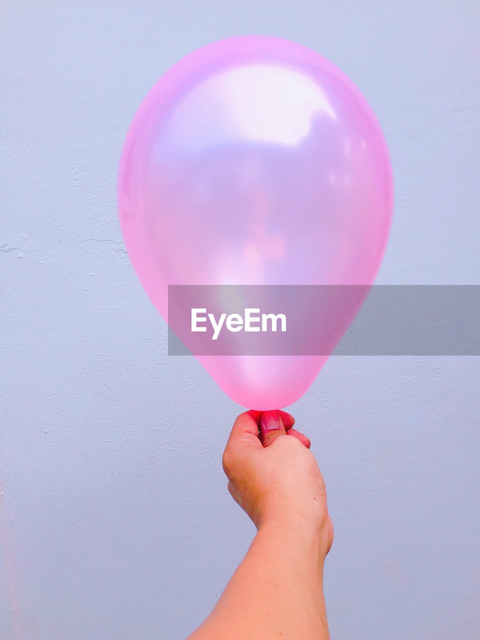 Cropped image of hand holding pink balloon against wall