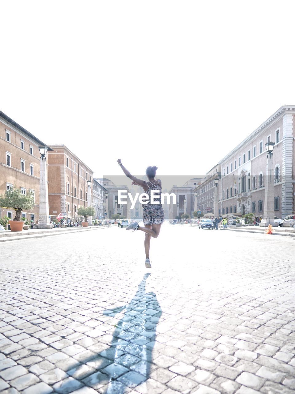Rear view of woman jumping on street against clear sky