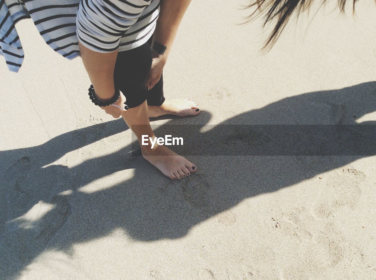 Low section of woman folding leggings while bending at beach