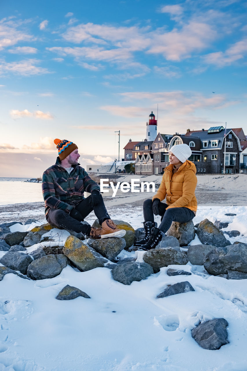 Couple sitting on rock against sky during winter