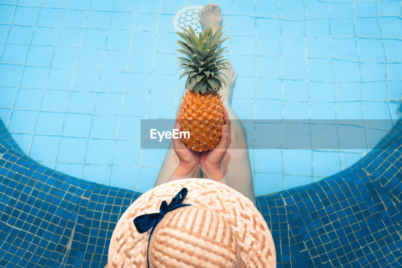 High angle view of woman holding pineapple while sitting in swimming pool