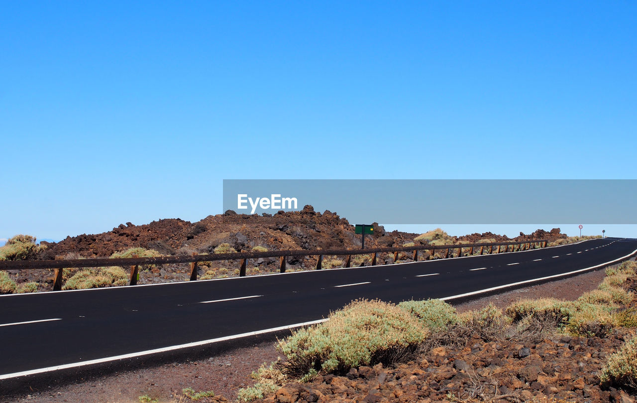 Road by landscape against clear blue sky