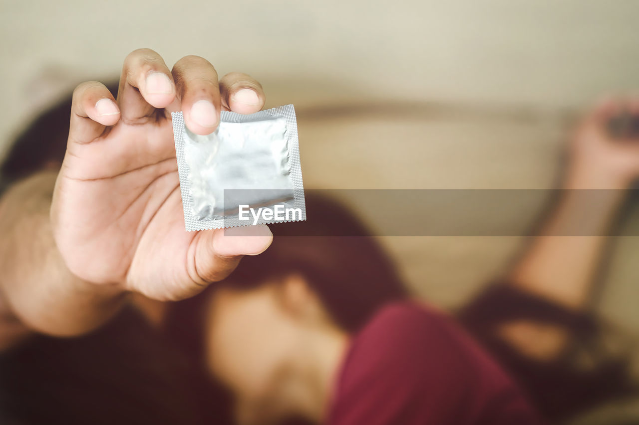 Close-up up couple holding condom lying on bed at home
