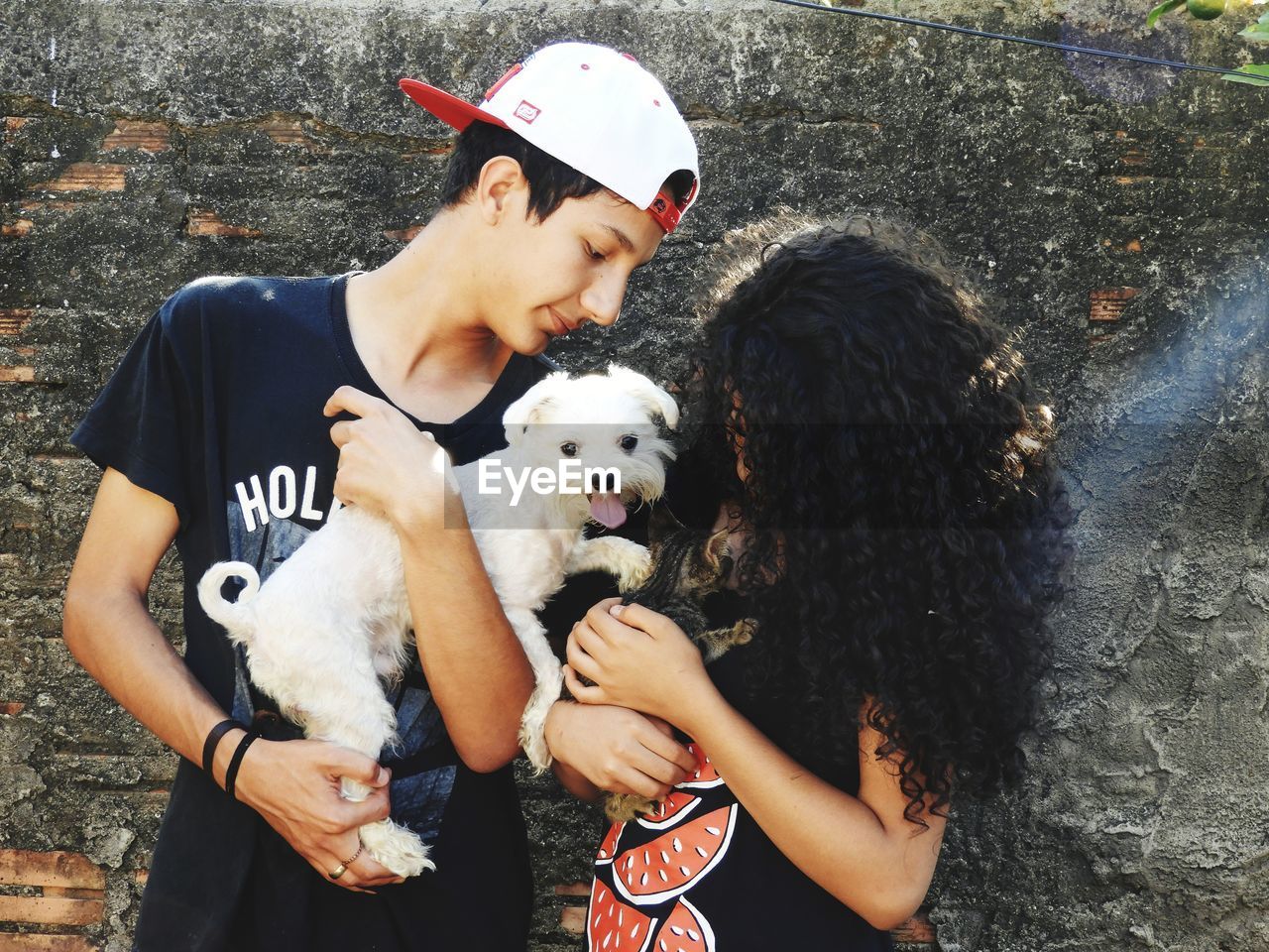 Teenage couple with dog and kitten standing against wall