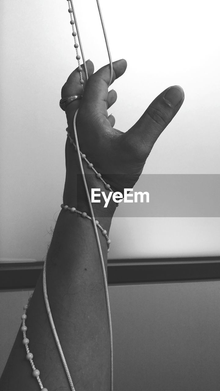 LOW ANGLE VIEW OF HUMAN HAND HOLDING HANGING AGAINST WALL