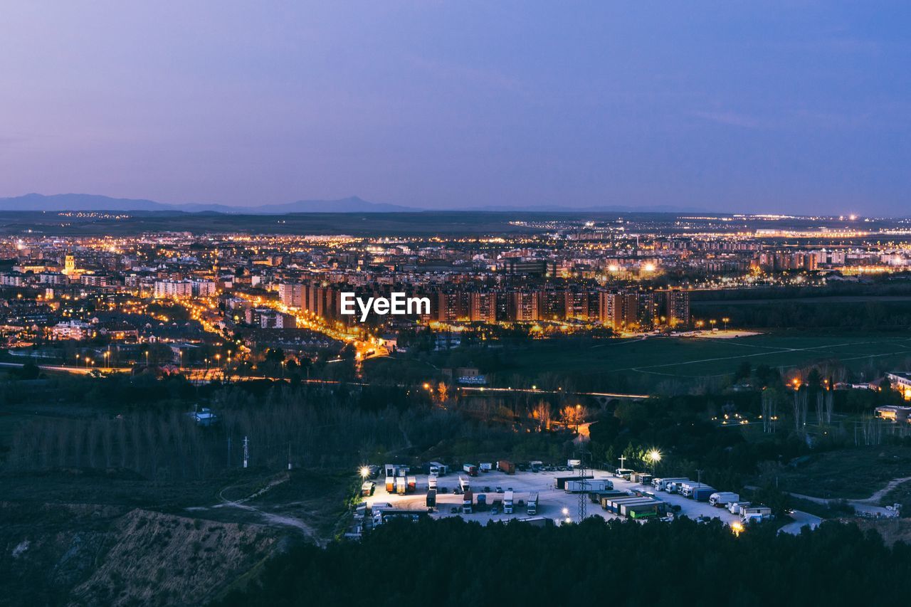 Illuminated cityscape by river against sky at night