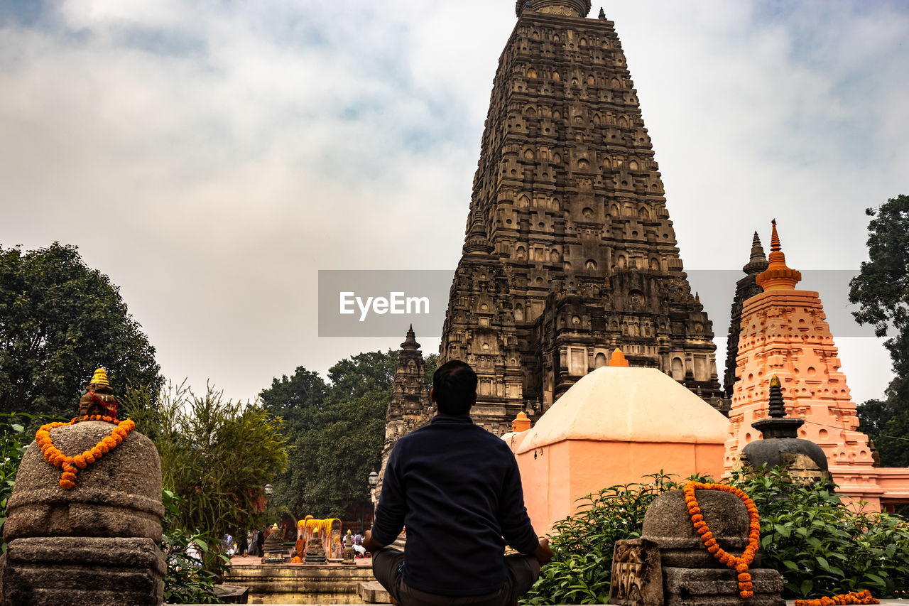 Rear view of man meditating while sitting outside temple