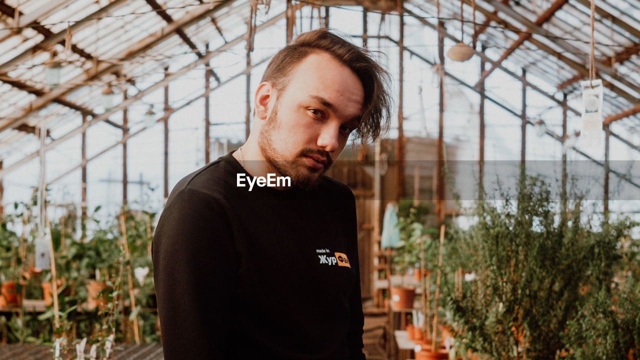 PORTRAIT OF YOUNG MAN LOOKING AT GREENHOUSE