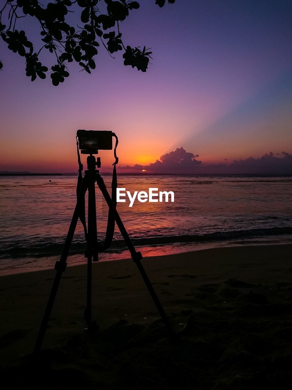 Silhouette camera on beach against sky during sunset