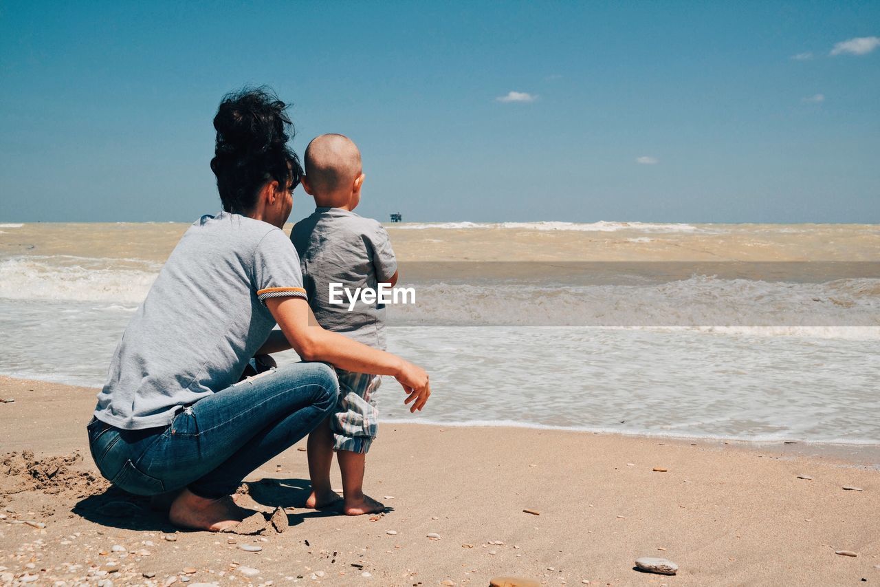 Mother with son at shore against sky