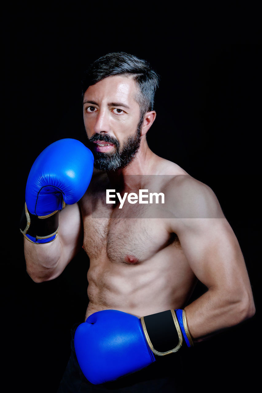 Portrait of boxer wearing boxing gloves standing against black background