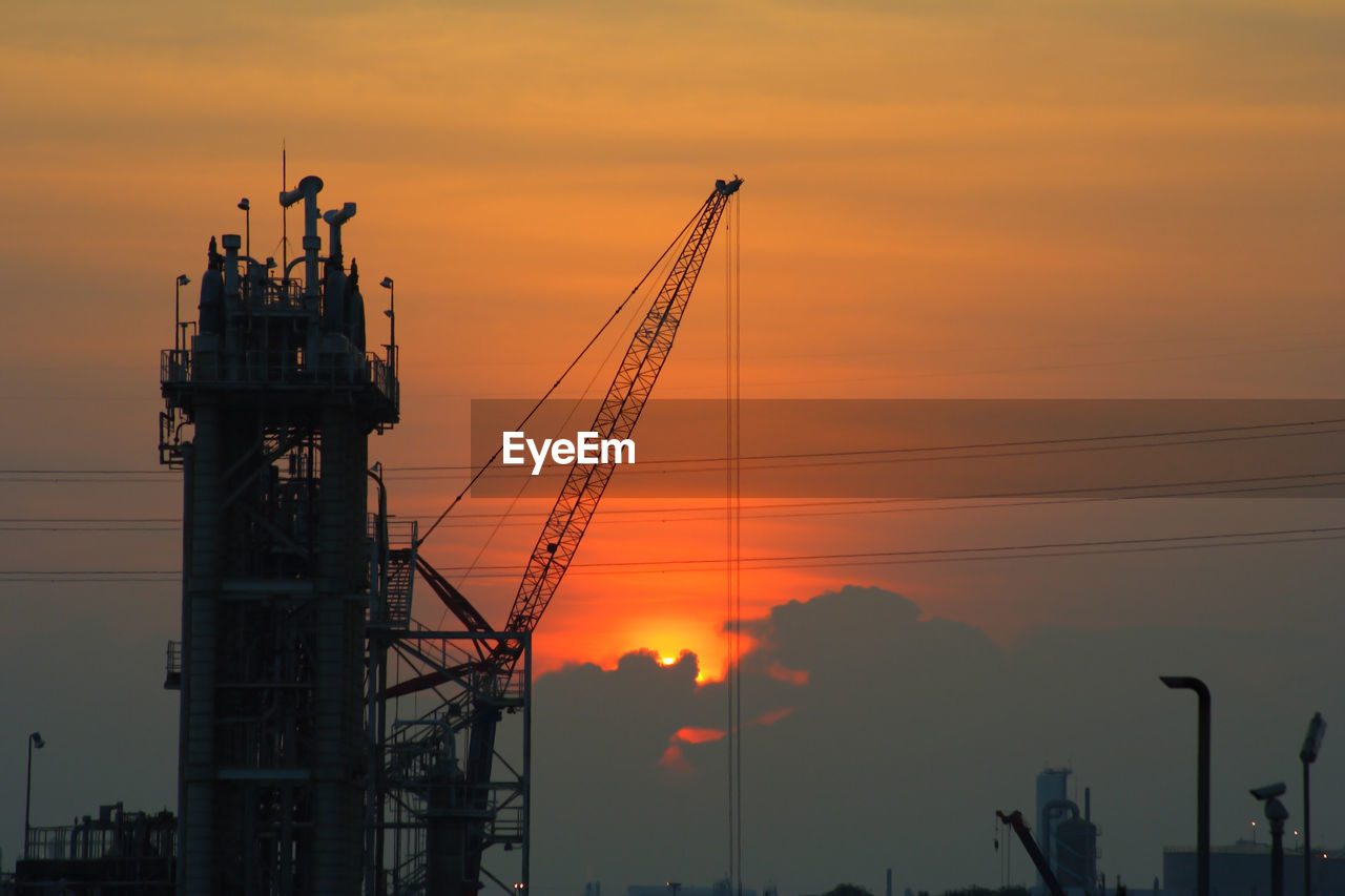 Silhouette cranes at construction site during sunset