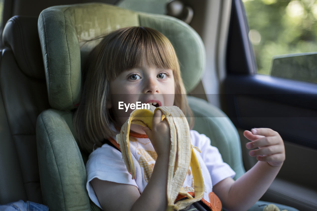 Portrait of cute girl eating a banana in car seat