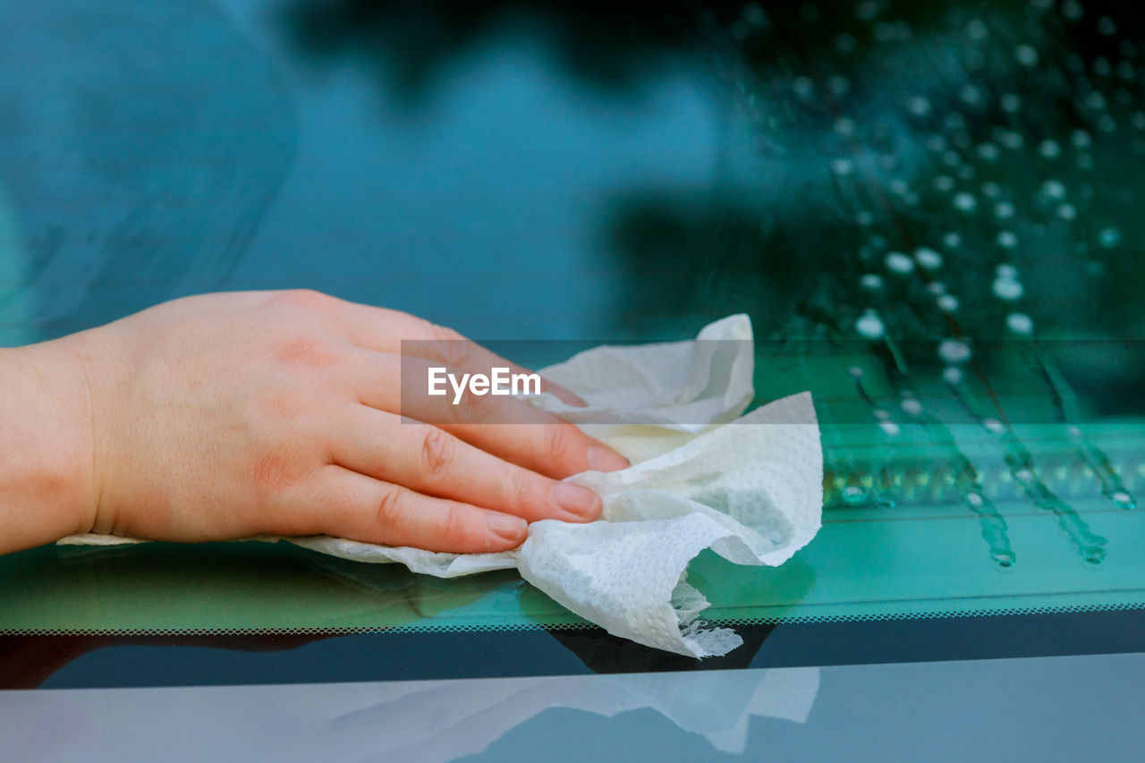 Cropped hand of woman cleaning car windshield