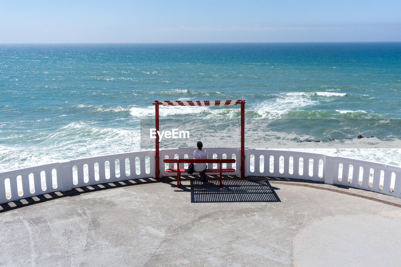 Woman sitting at beach against clear sky