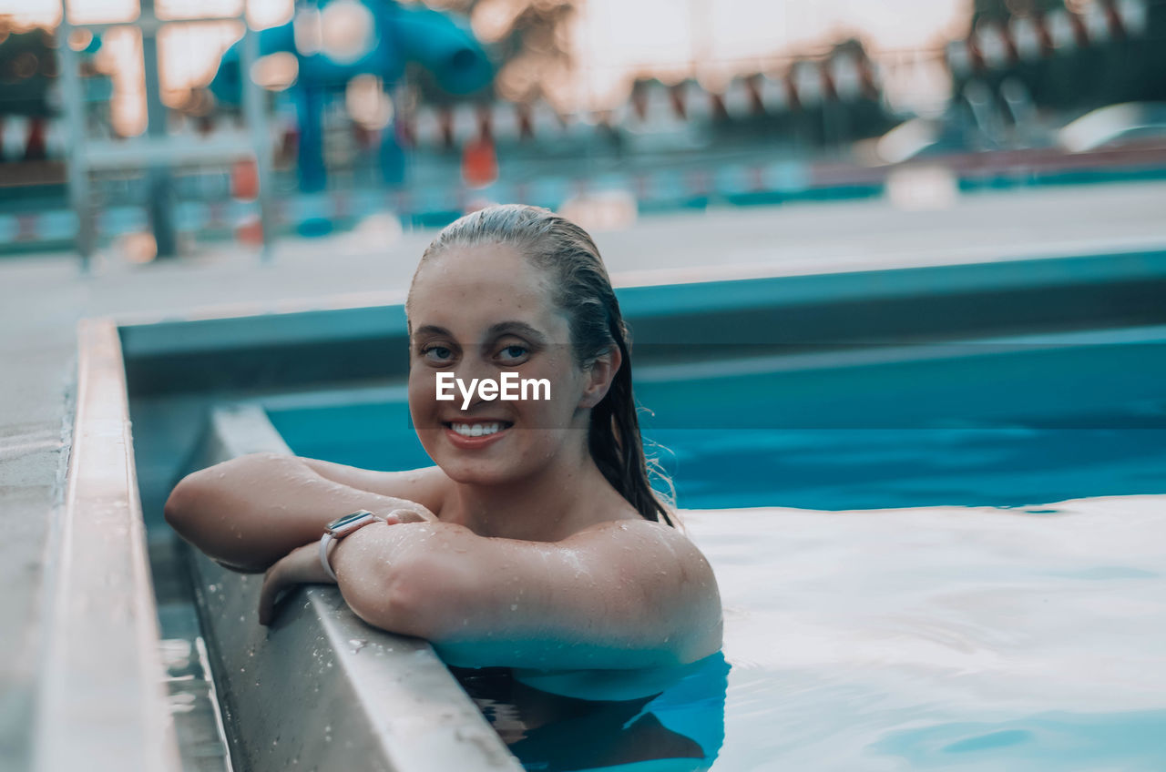 PORTRAIT OF SMILING YOUNG WOMAN SWIMMING POOL