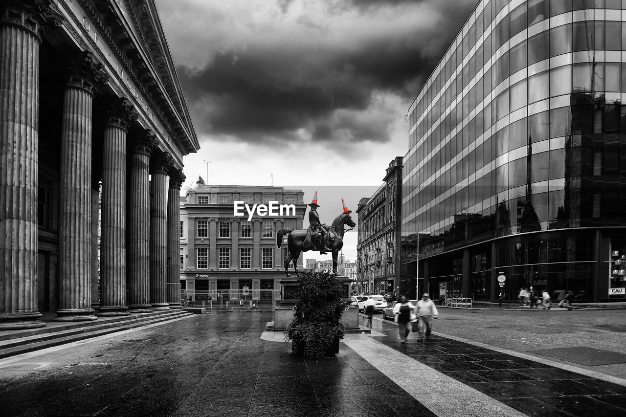 PEOPLE WALKING ON STREET BY BUILDINGS AGAINST SKY