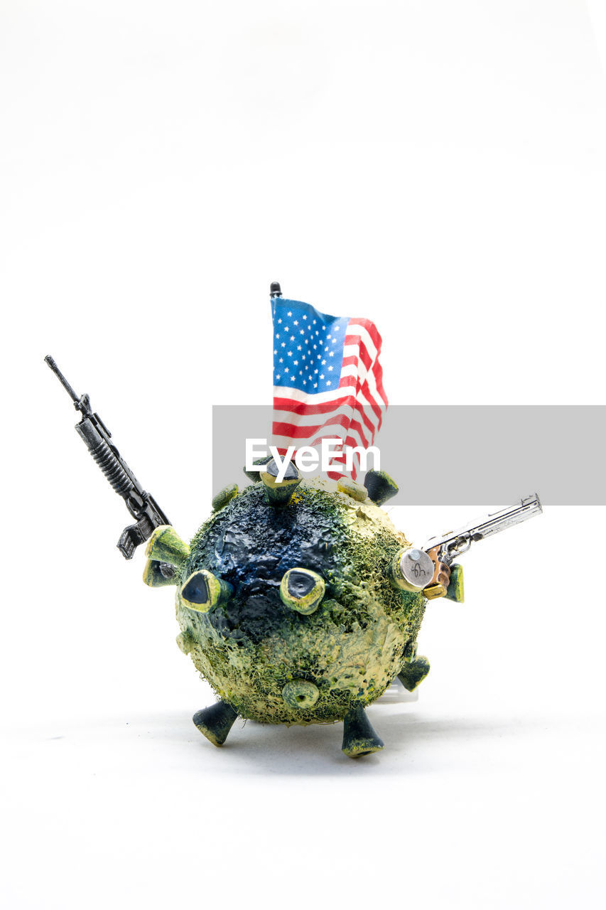 Close-up of coronavirus model with guns and flag on white background