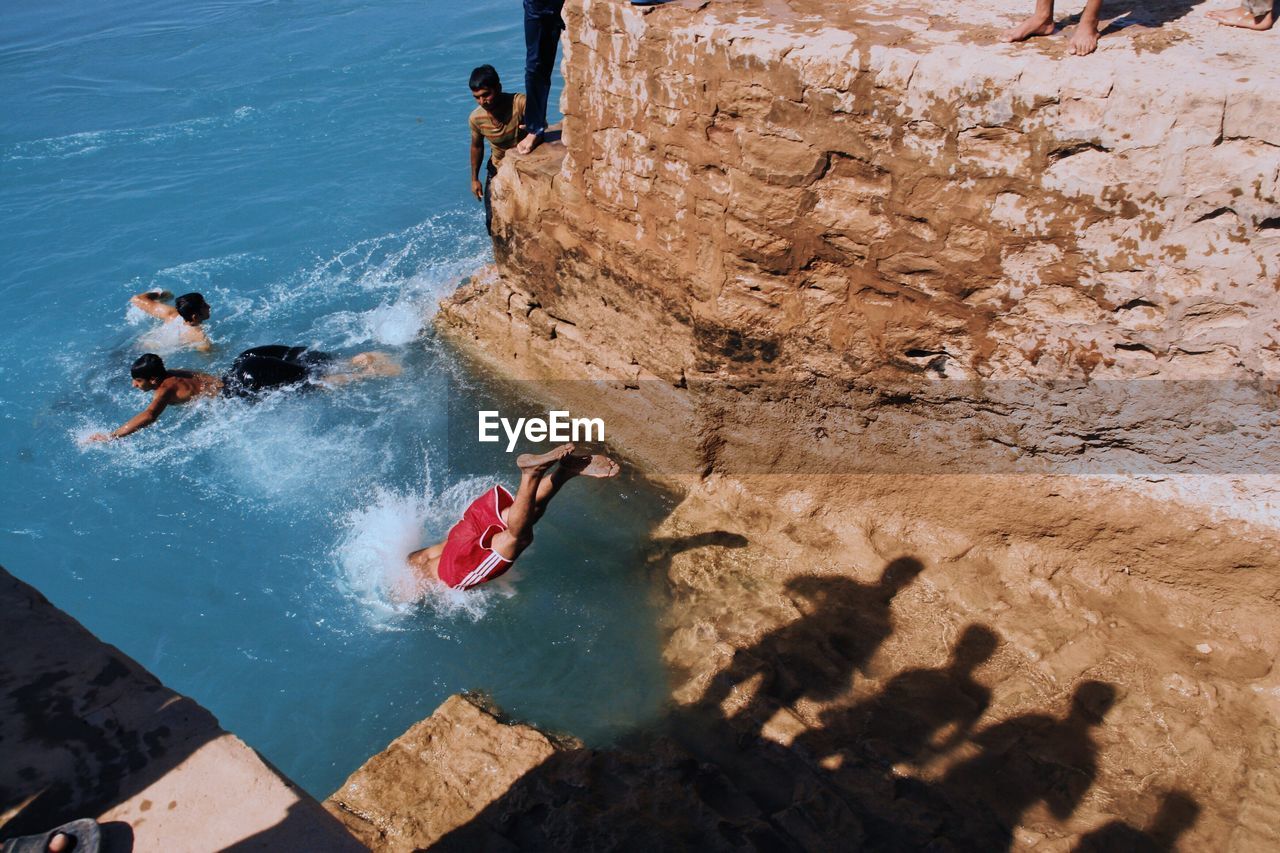 HIGH ANGLE VIEW OF MAN SURFING ON ROCKS