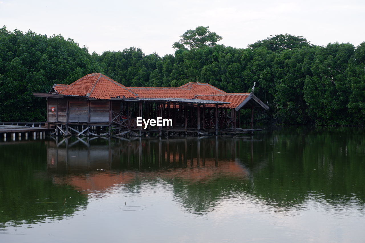 House by lake against trees and sky