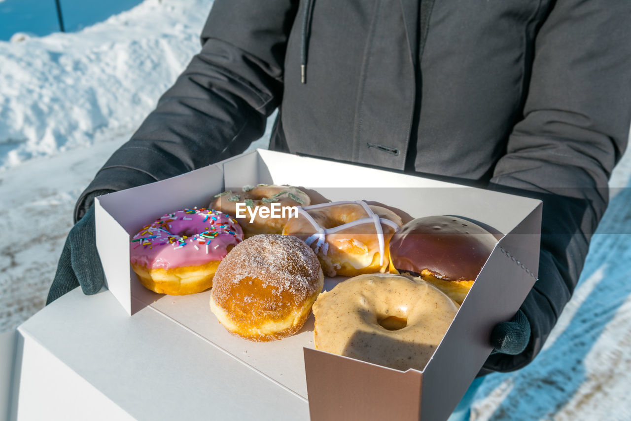 Midsection of woman holding fresh donuts in cardboard box during winter