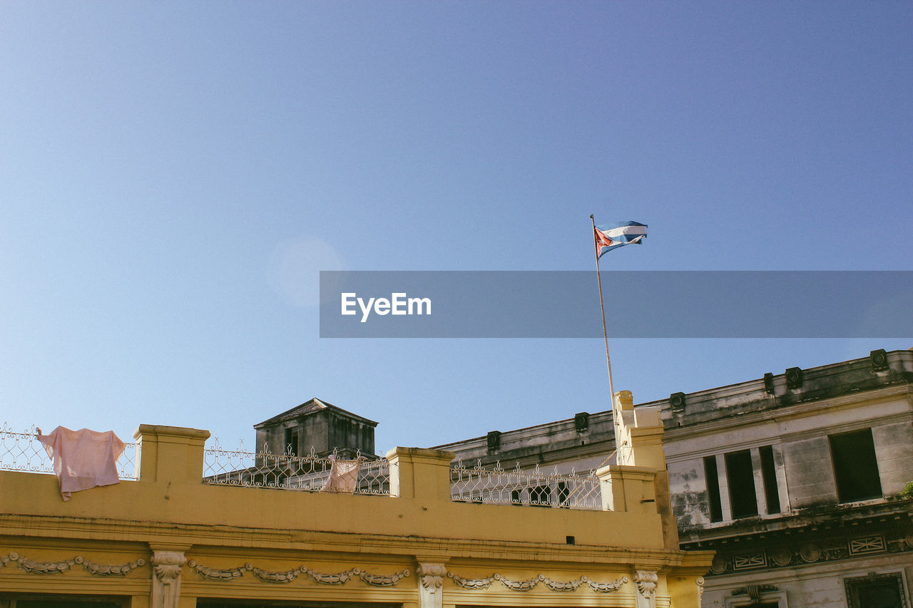 Low angle view of cuban flag on hotel building against clear blue sky