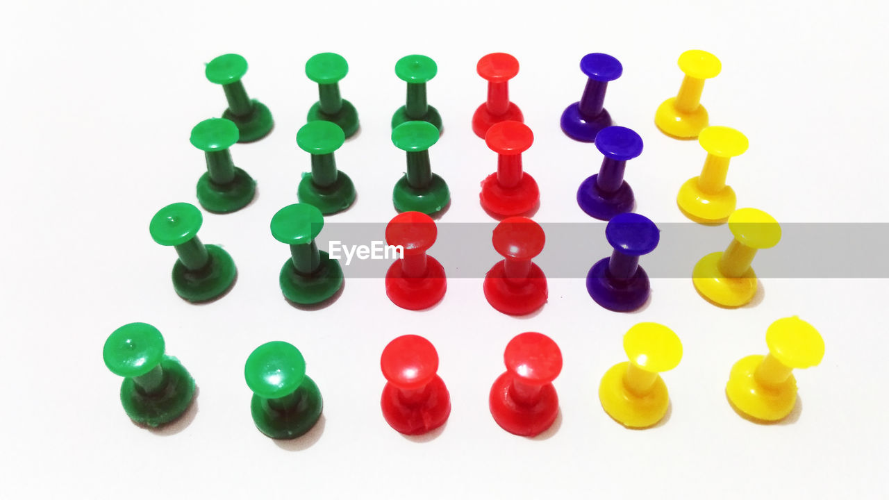 High angle view of multi colored thumbtacks against white background