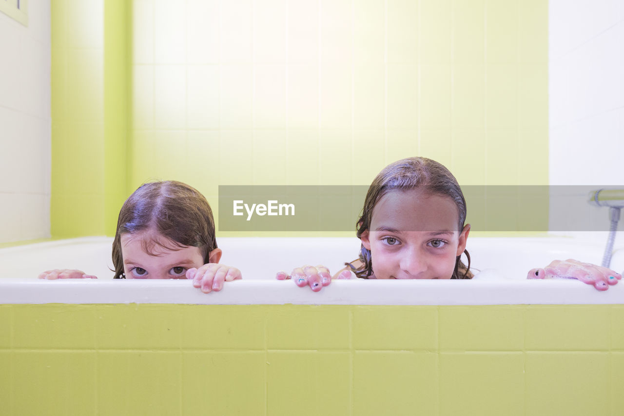 Portrait of siblings taking bath in tub at bathroom