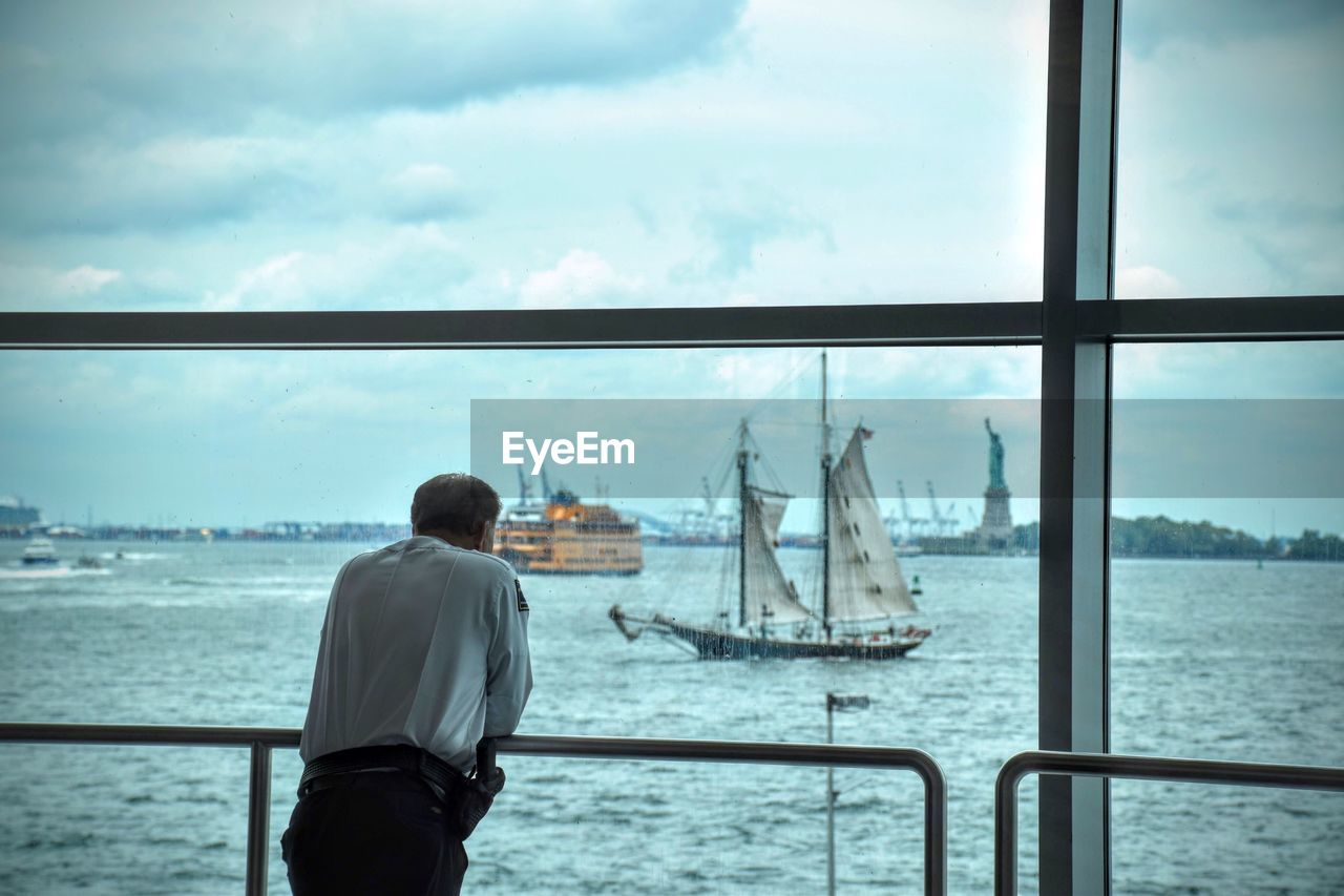 REAR VIEW OF MAN STANDING ON SEA