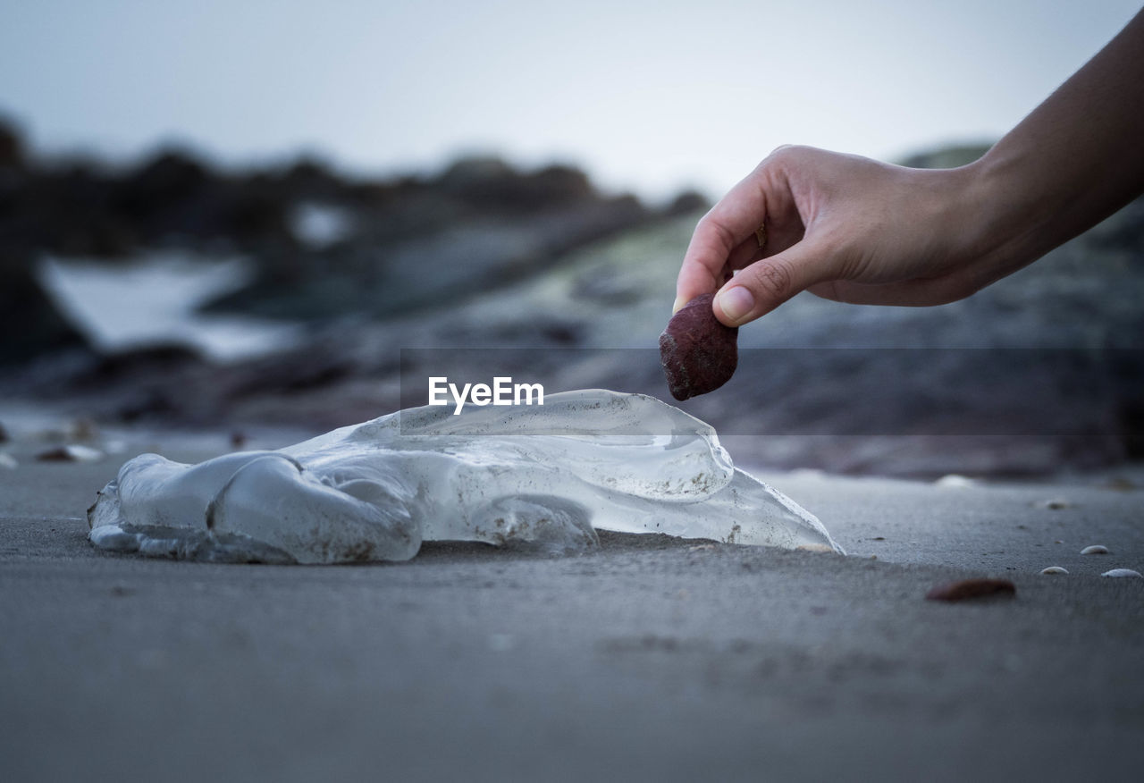 Cropped image of hand holding stone over ice at beach