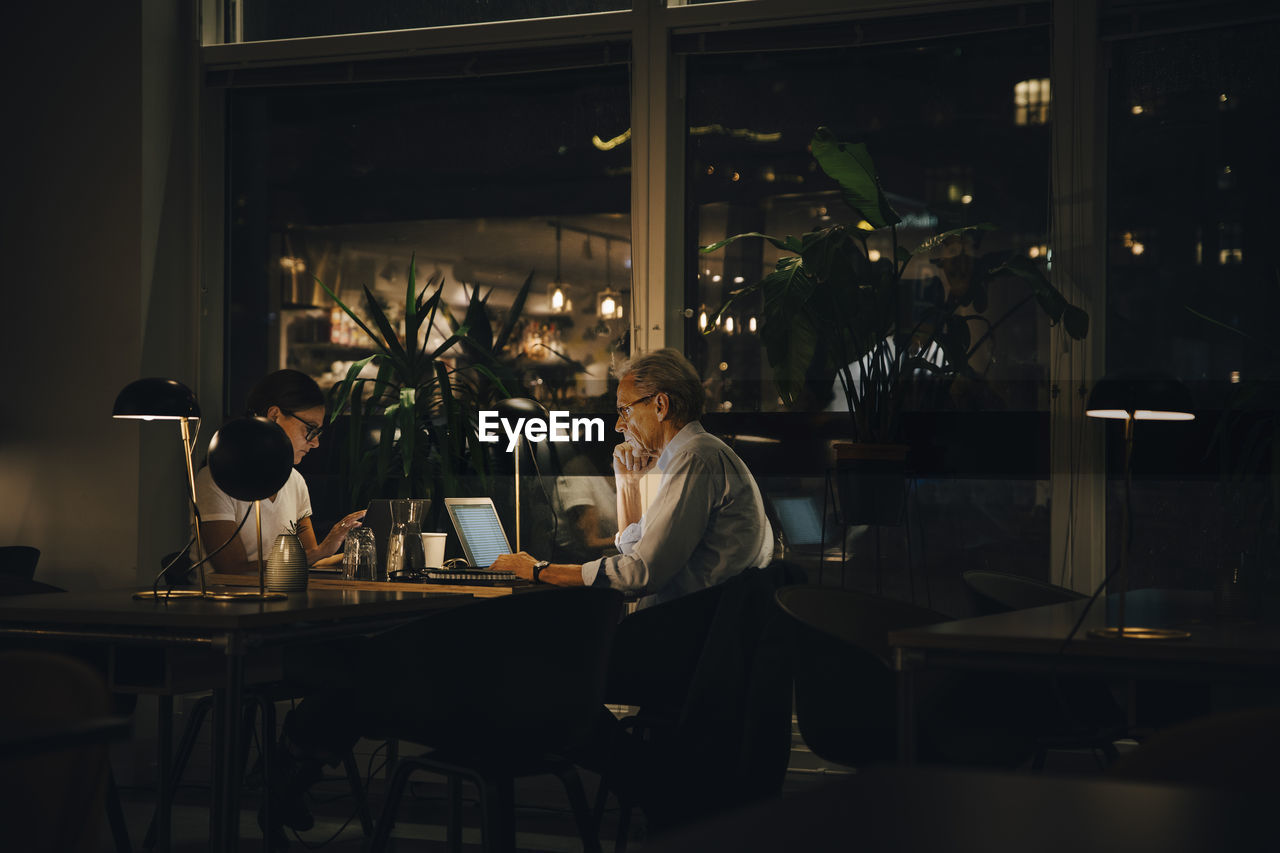 Male and female professionals working late in dark office at night