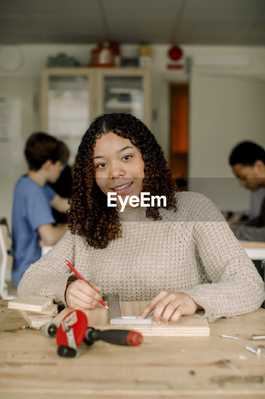 Portrait of female teenage student with ruler and pencil during carpentry class at high school