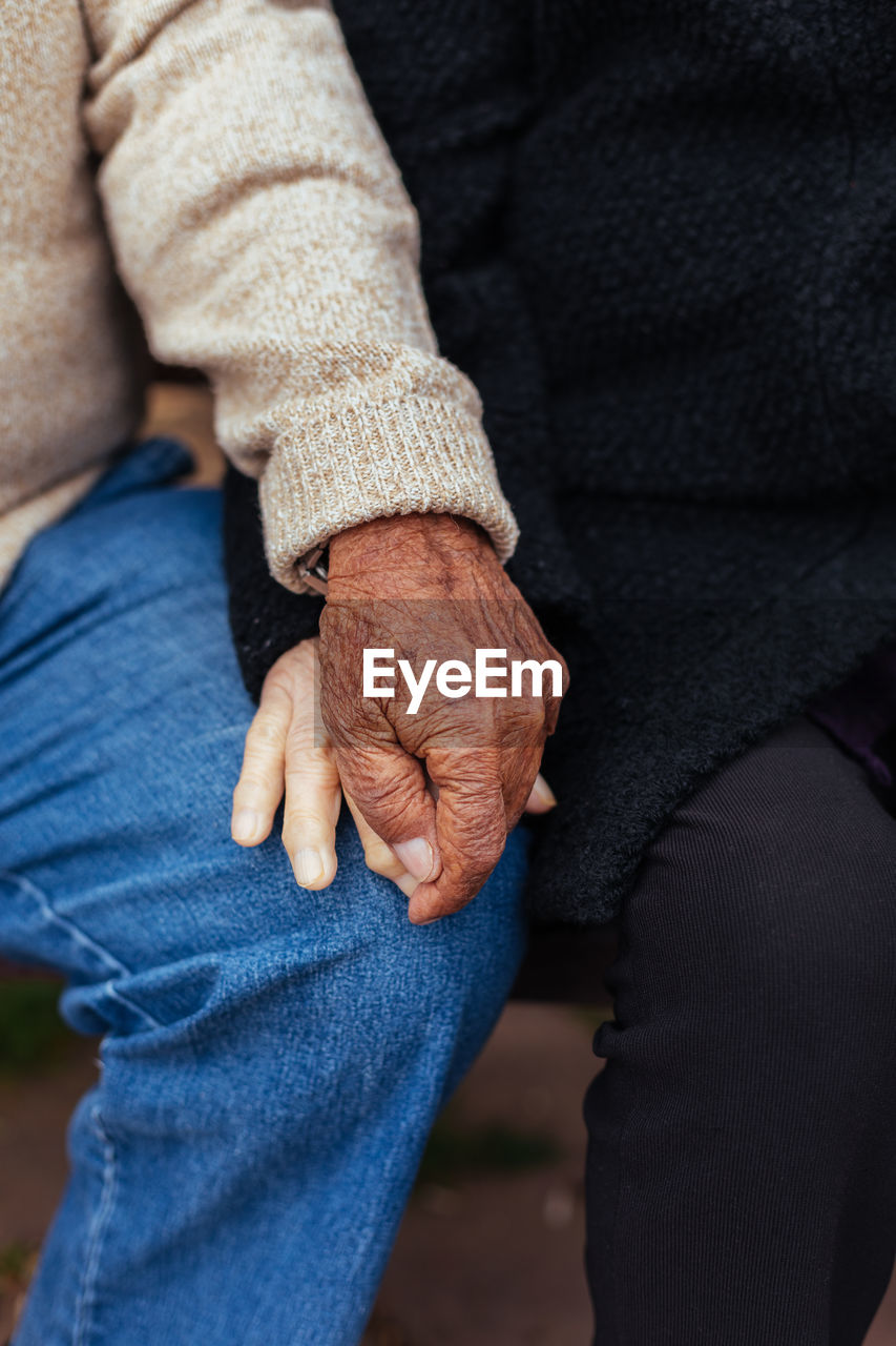 Crop of anonymous elderly couple holding hands while sitting on a park bench