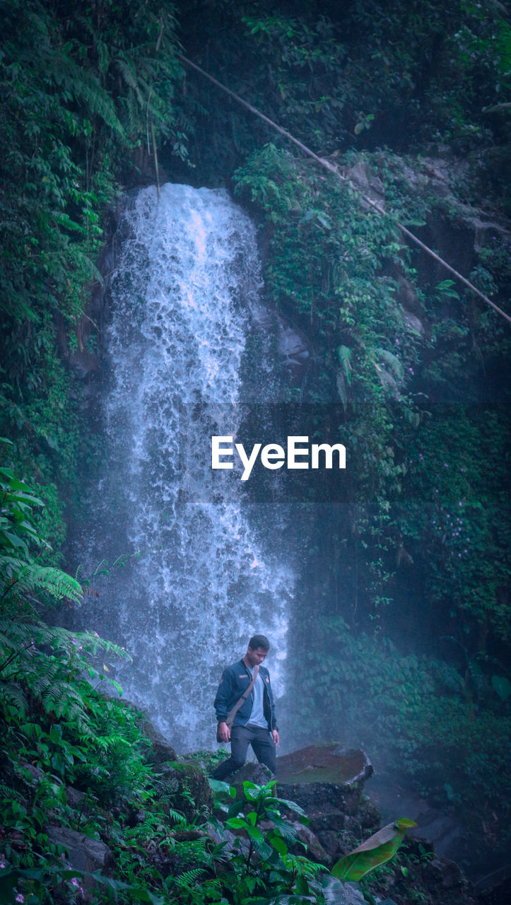 Man looking down while standing against waterfall