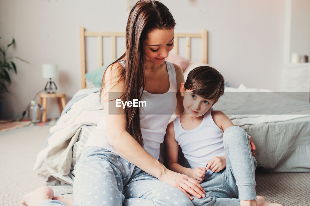 Portrait of boy with mother sitting in bedroom at home