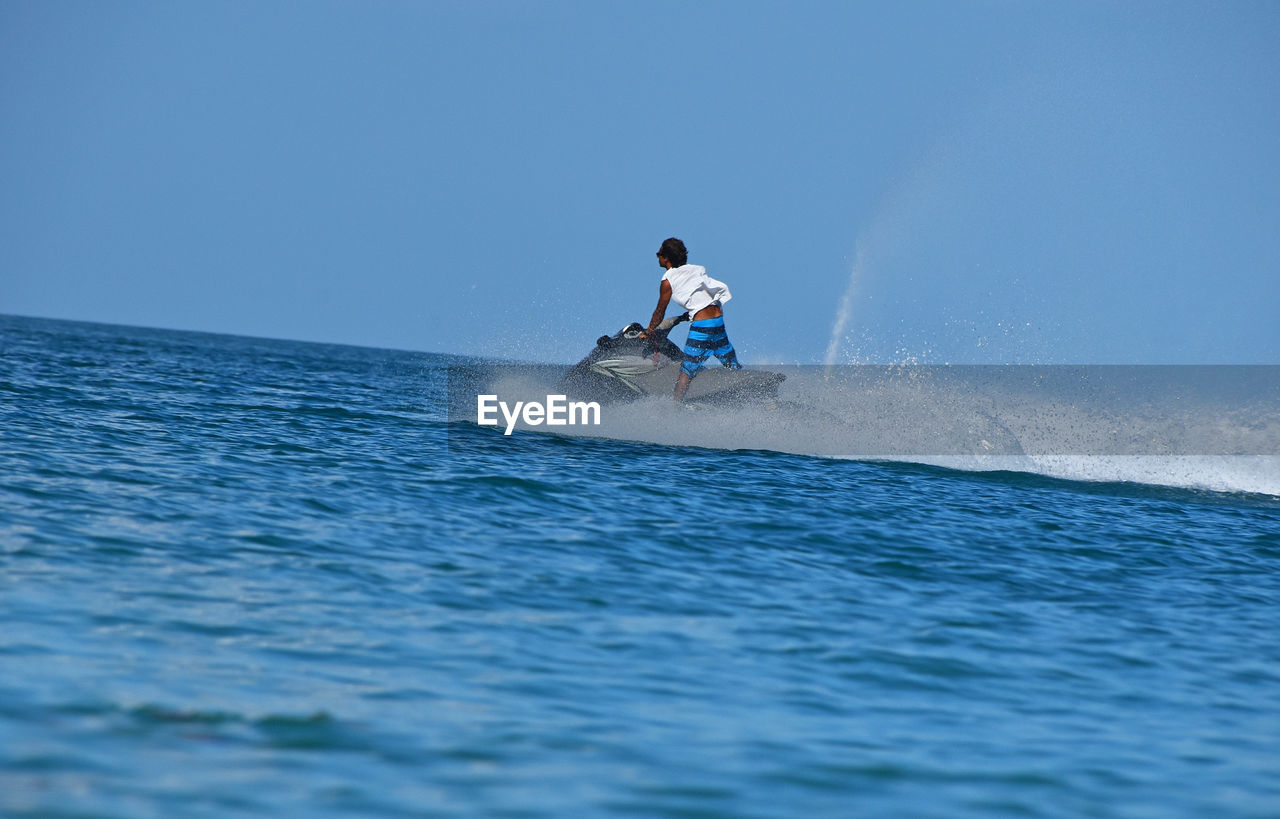 Rear view of man on jet boat over sea against clear sky